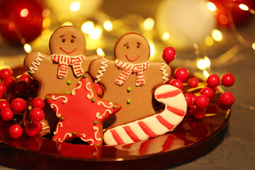 Plate with Christmas gingerbread cookies and rowan on table against blurred lights