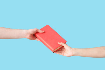 Hand passing book to another person on pink background