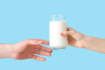 Hands handing over glass of milk on blue background