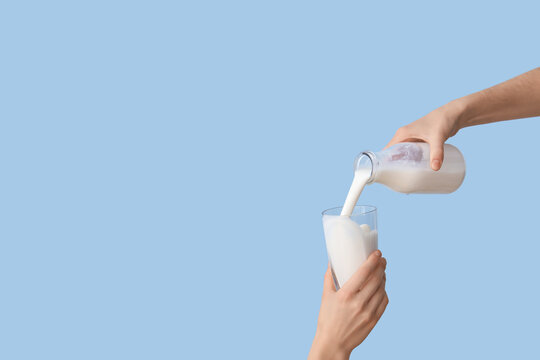Hands pouring milk from bottle into glass on light blue background