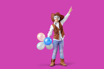 Funny little boy in cowboy costume and carnival mask pointing at something on purple background