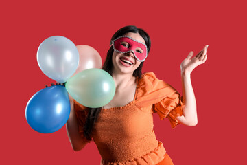 Happy young woman in carnival mask with balloons on red background