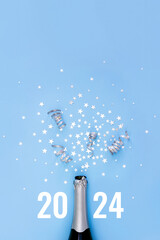 Open bottle of champagne on blue background decorated with silver star confetti and numbers 2024....