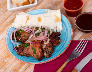 Appetizing spicy pork shashlik with fresh onion and greens served with lavash and sauces. Traditional Caucasian cuisine