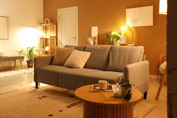 Interior of modern living room with grey sofa and glowing lamps at evening