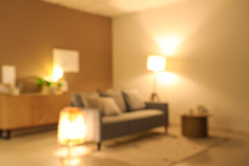 Blurred view of modern living room with grey sofa and glowing lamps at evening