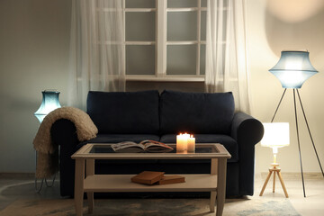 Interior of modern living room with black sofa, coffee table and glowing lamps at evening