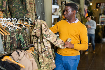 Adult male shopper chooses camouflage uniform at army store