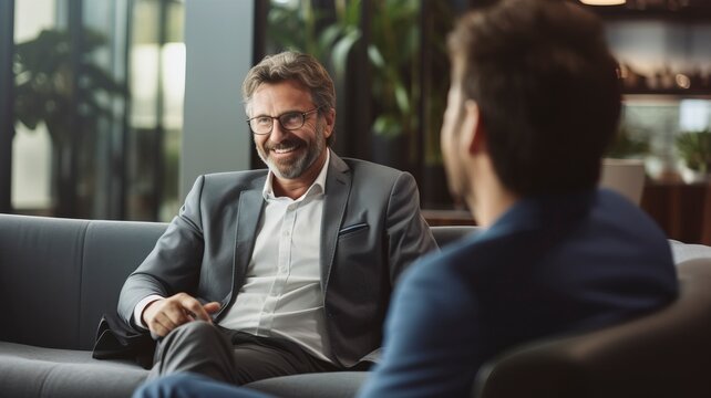 Mature businessman talking with younger colleague on couch with generative ai