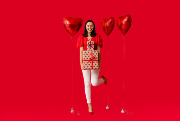 Beautiful young woman with air balloons in shape of heart and gift boxes on red background....