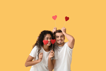 Funny young couple with red hearts for Valentine's day on yellow background