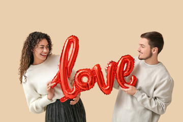 Young couple with air balloon in shape of word LOVE for Valentine's day on beige background