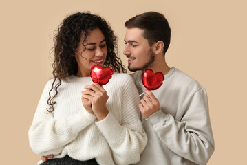 Young couple with air balloons in shape of heart for Valentine's day on beige background