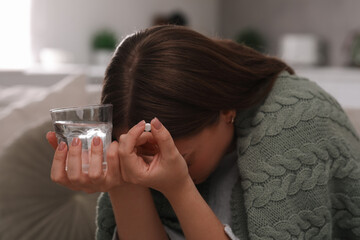 Depressed woman with antidepressant pill and glass of water indoors