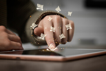 Woman using tablet for online purchases at table, closeup. Shopping cart icons flying out of device...