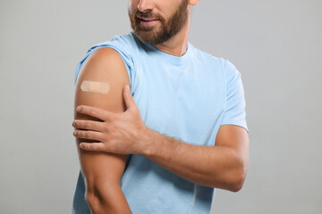 Man with sticking plaster on arm after vaccination against light grey background, closeup