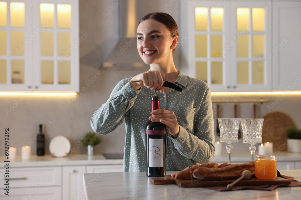 Wall mural Romantic dinner. Woman opening wine bottle with corkscrew at table in kitchen