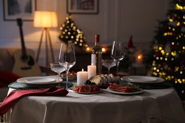 Christmas table setting with burning candles, appetizers and dishware in room