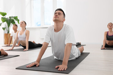 Obraz premium Young man practicing yoga during group lesson indoors
