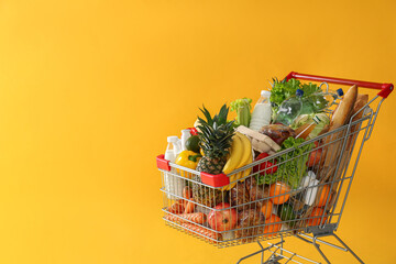 Shopping cart full of groceries on yellow background. Space for text