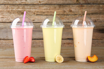 Plastic cups with different tasty smoothies and fresh fruits on wooden table
