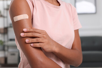 Young woman with adhesive bandage on her arm after vaccination indoors, closeup