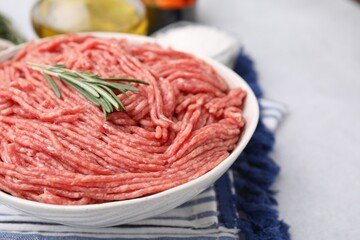 Fresh raw ground meat and rosemary in bowl on light table, closeup