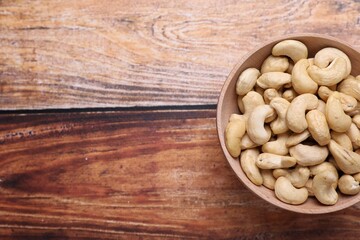 Tasty cashew nuts in bowl on wooden table, top view. Space for text