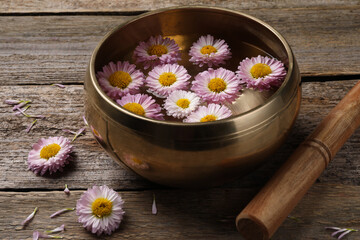 Tibetan singing bowl with water, chrysanthemum flowers and mallet on wooden table