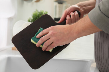 Man washing dark wooden cutting board at sink in kitchen, closeup