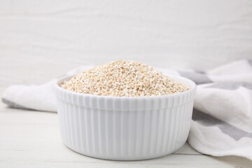 Dry barley groats in bowl on white wooden table, closeup