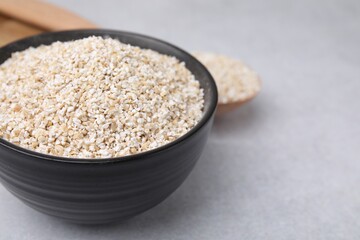 Dry barley groats in bowl on light grey table, closeup. Space for text