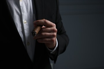 Man smoking cigar on dark grey background, closeup. Space for text