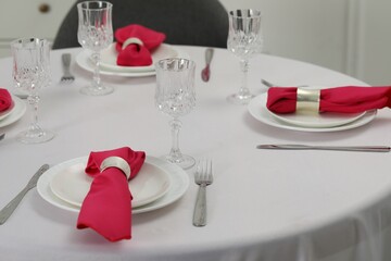 Color accent table setting. Glasses, plates, cutlery and pink napkins on table indoors