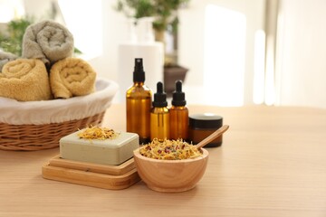 Fototapeta na wymiar Soap bar, dry flowers, bottles of essential oils, jar with cream and towels on wooden table indoors, space for text. Spa time