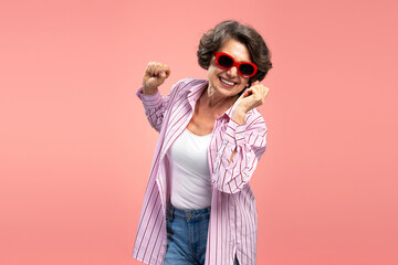 Smiling senior woman, happy funny grandmother wearing stylish pink shirt dancing, having fun isolated on background  - obrazy, fototapety, plakaty