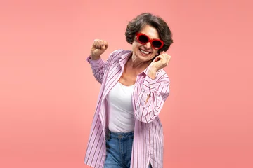 Fotobehang Smiling senior woman, happy funny grandmother wearing stylish pink shirt dancing, having fun isolated on background  © Maria Vitkovska
