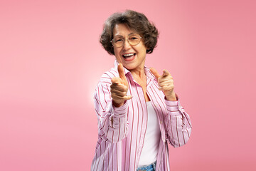 Excited senior woman, happy funny grandmother wearing eyeglasses and stylish pink shirt dancing,...