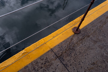 Cement Walkway with a Yellow Edge and Wire Railing Above a Harbor.