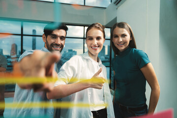 Happy businesspeople pointing at glass wall while standing with confident. Group of businesspeople...