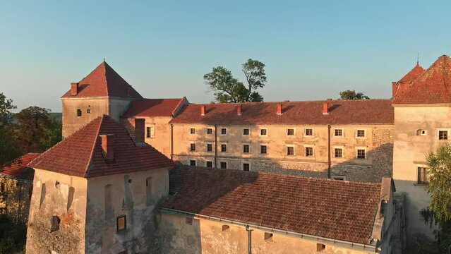 Amazing drone close-up footage circling an ancient fortress. Bathed in warm sunset hues, admire gray and yellow walls complemented by brown and dark orange roof tiles.