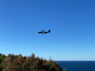 Fototapeta na wymiar Airplane in the sky. Aircraft in the sky over the mountains. A black plane takes off from an ocean coast.