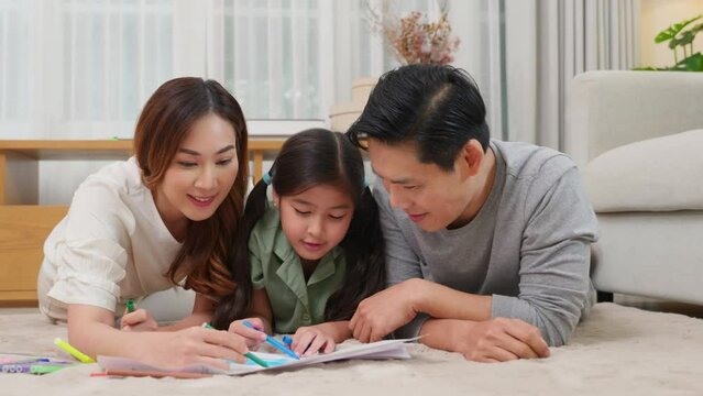 Smiling Father, Mother and daughter drawing together on paper at home, Asian family lying on floor painting with child daughter in living room, Happy family activity enjoy, learning draw art picture