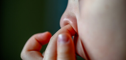 Caucasian young child picking their nose with an index finger