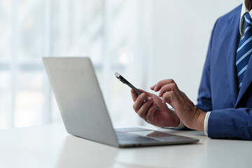 Businessman holds smartphone, checks email, checks job details on Laptop computer on white desk to point to successful business goals in office.