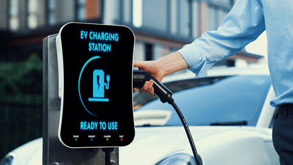 Businessman recharge his electric car from charging station at city center or public car park. Eco...
