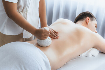Hot herbal ball spa massage body treatment, masseur gently compresses herb bag on man body....