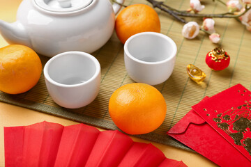 Teapot with cups, Japanese envelopes and mandarins on yellow background. New Year celebration