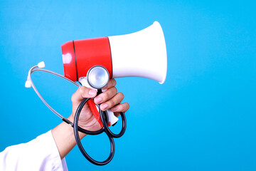 Close up doctor's hand holding stethoscope and megaphones over blue background