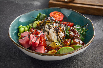 Fresh tuna poke bowl with ripe avocado, edamame beans, and rice, garnished with seaweed, in a...